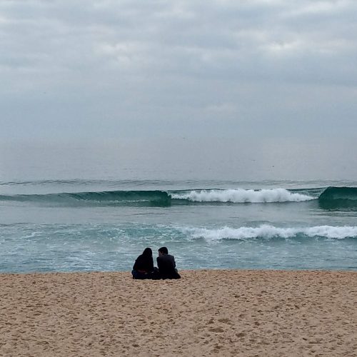 Zwei Personen sitzen an einem wilden Sandstrand an der Westküste Portugals