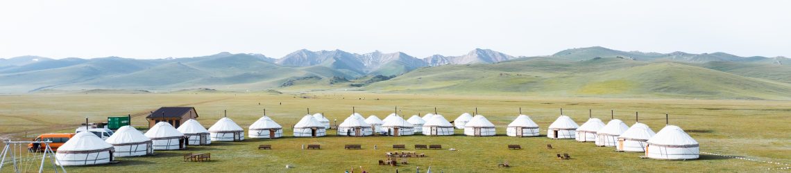 Jurten auf einer Bergwiesen vor einem Gipfepanorama