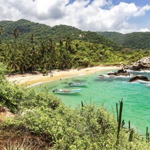 Nationalparl von Tayrona. Üooig bewachsene Sandbucht mit kleinen Booten